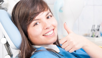 A young woman giving a thumbs up in the dentist chair 