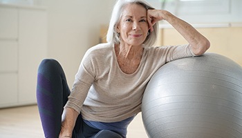 Senior woman smiling while resting against balance ball