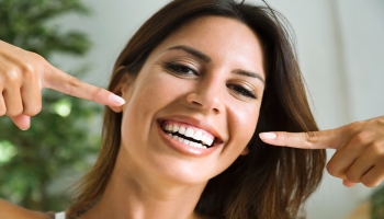 Alt image tag: Woman pointing to her beautiful smile with dental implants in Danville