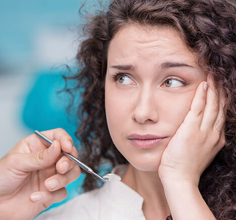 Woman in dental chair holding her jaw in pain