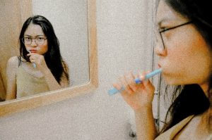 Woman brushing her teeth and looking in the mirror.