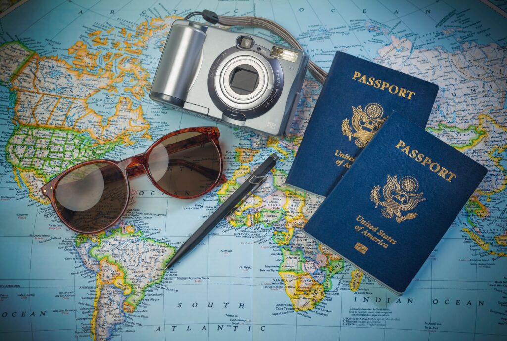 Two passports, sunglasses, camera, and pen on map of the world